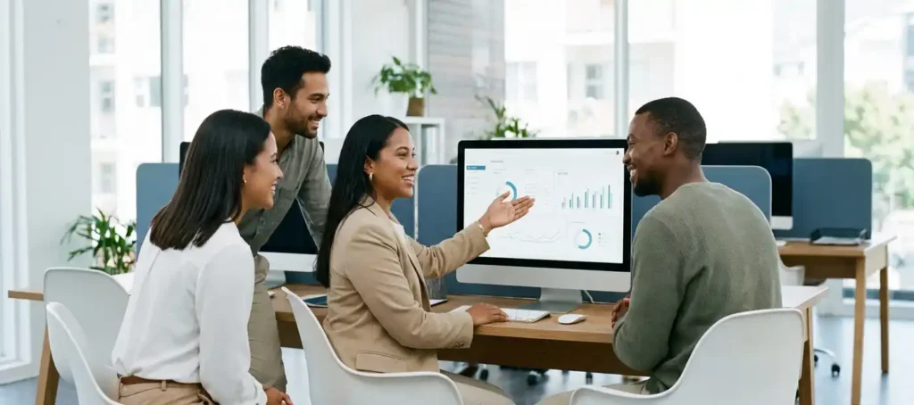 Teamleider begeleidt collega's bij een moderne werkplek met dashboardinterface op monitor, open kantoor met natuurlijk licht.