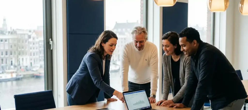 Vier collega's rond een vergadertafel in een modern Nederlands kantoor, één persoon presenteert laptop aan aandachtig team in warm natuurlijk daglicht.